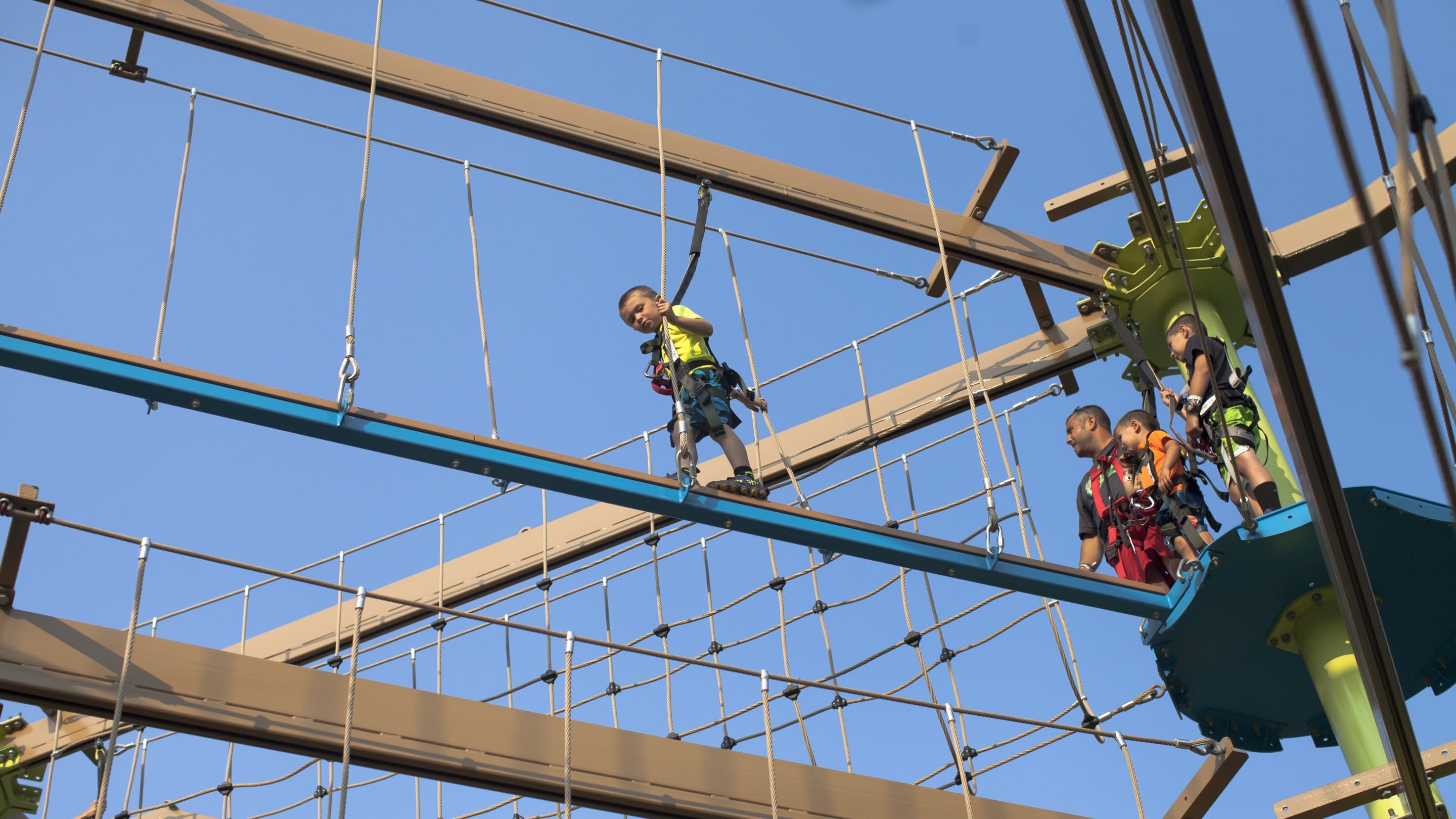 Kids and adults in harnesses on high ropes course under clear blue sky