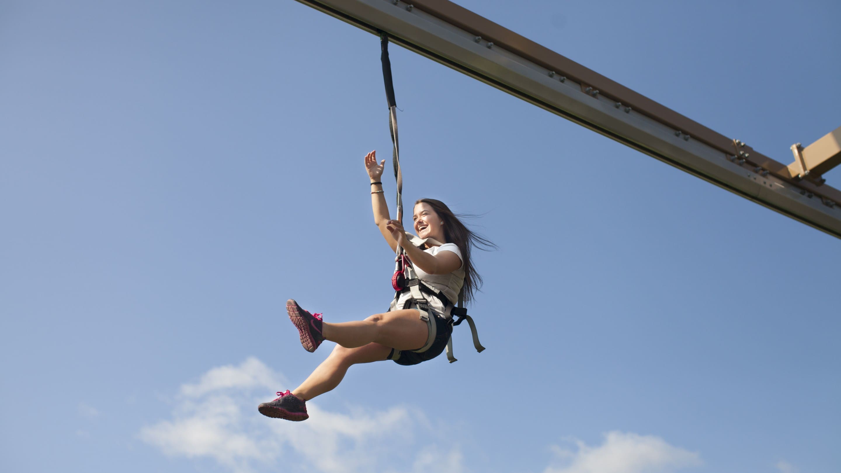 Smiling woman rides zip line against clear blue sky