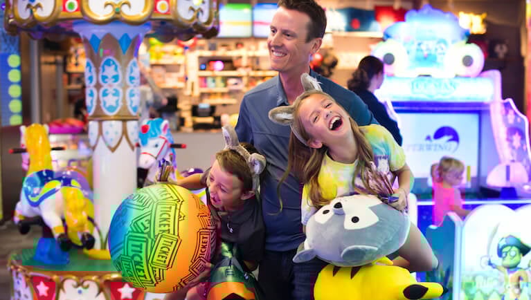 father carrying two laughing kids with prizes won at arcade counter