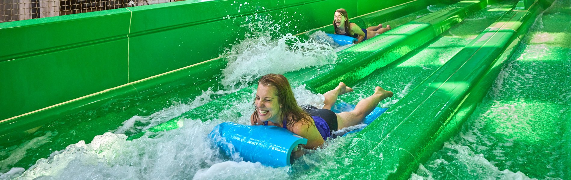 two girl friends going down a green water park slide
