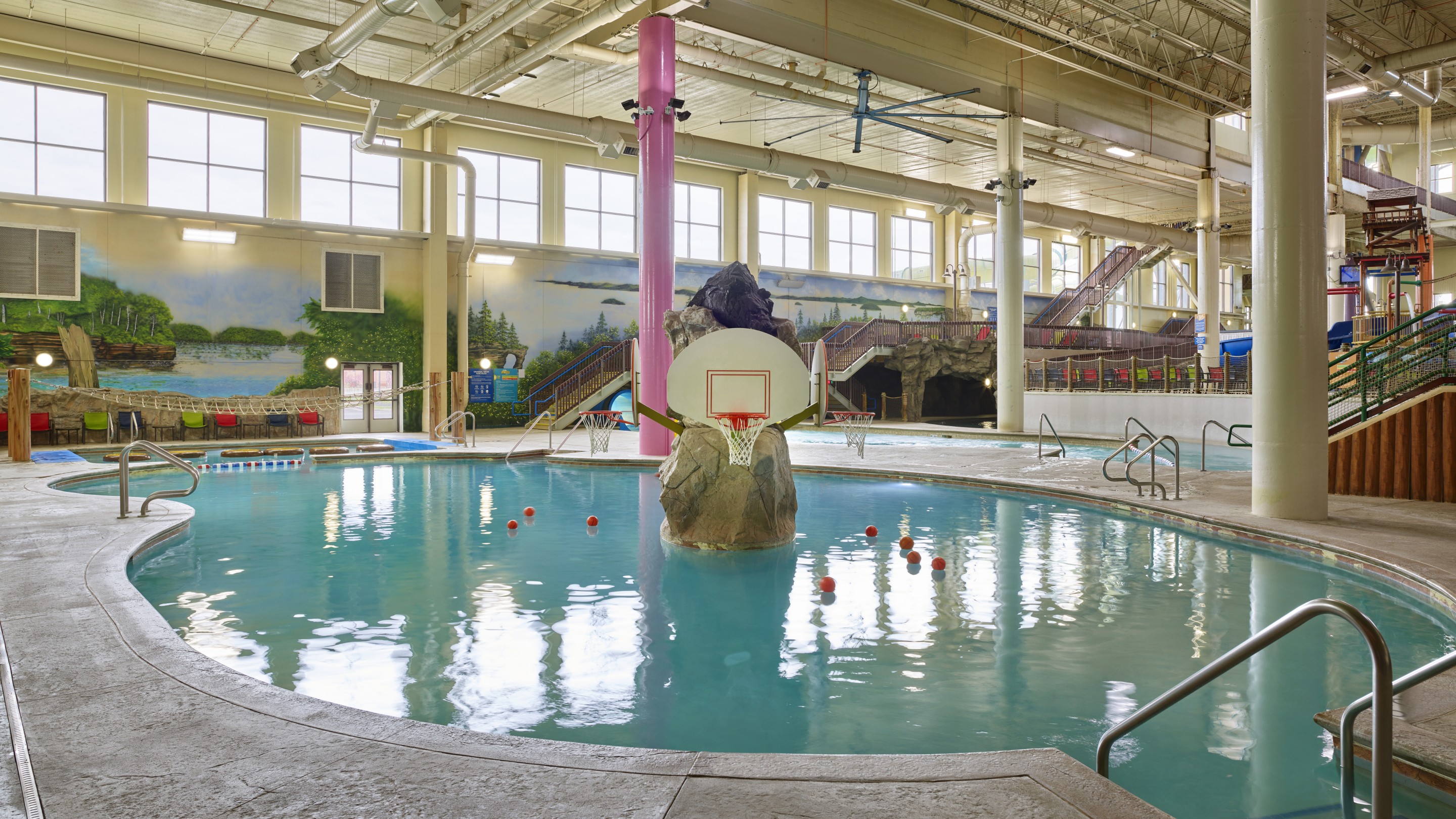 A spacious indoor pool featuring a basketball hoop and a fun water slide for fun activities.