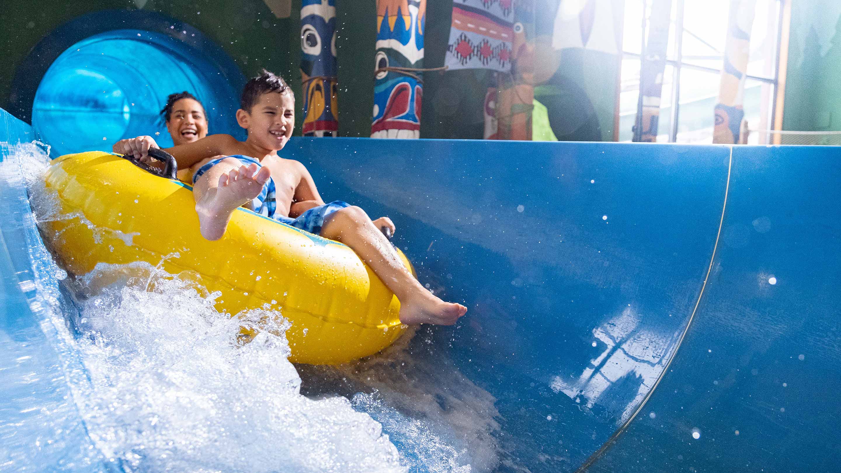 Two people on a yellow inner tube racing down a blue water slide.