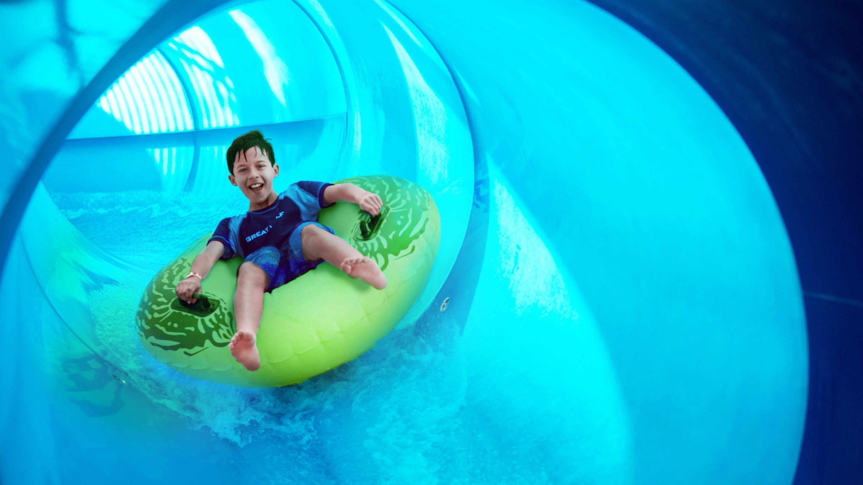 Boy rides down blue waterslide on yellow tube 