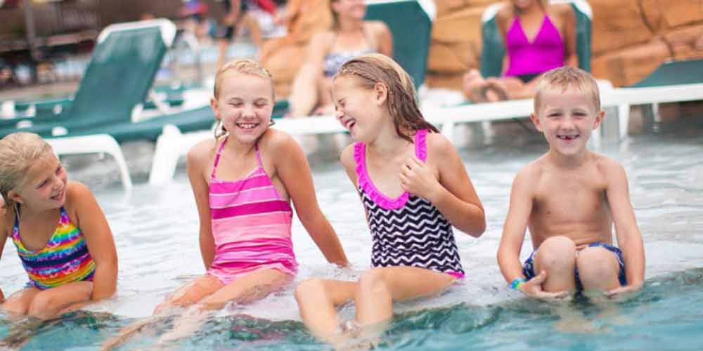 Four kids relax at the edge of an outdoor pool at Great Wolf Lodge indoor water park and resort.