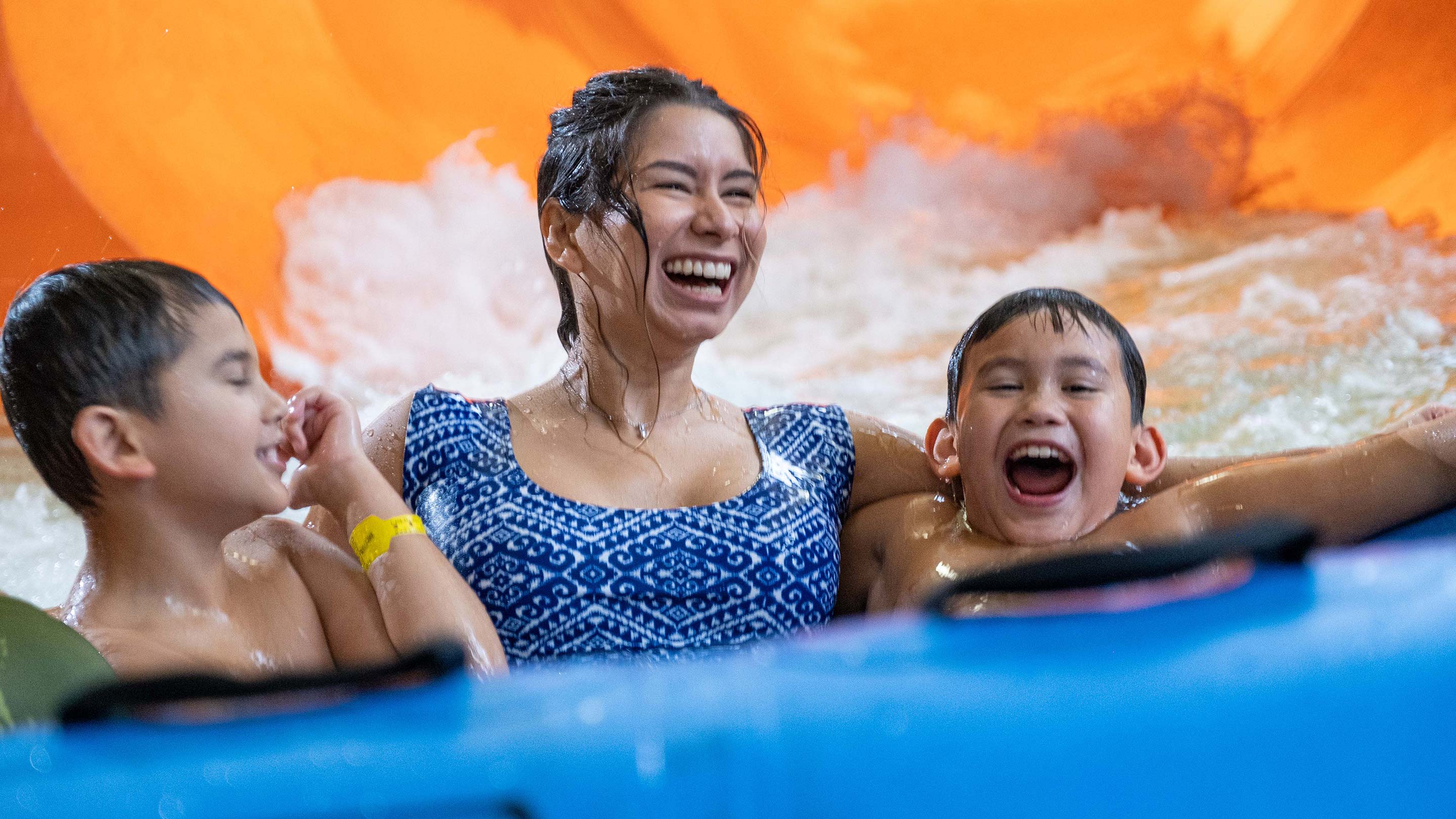 A woman and two young boys on a blue raft slide.