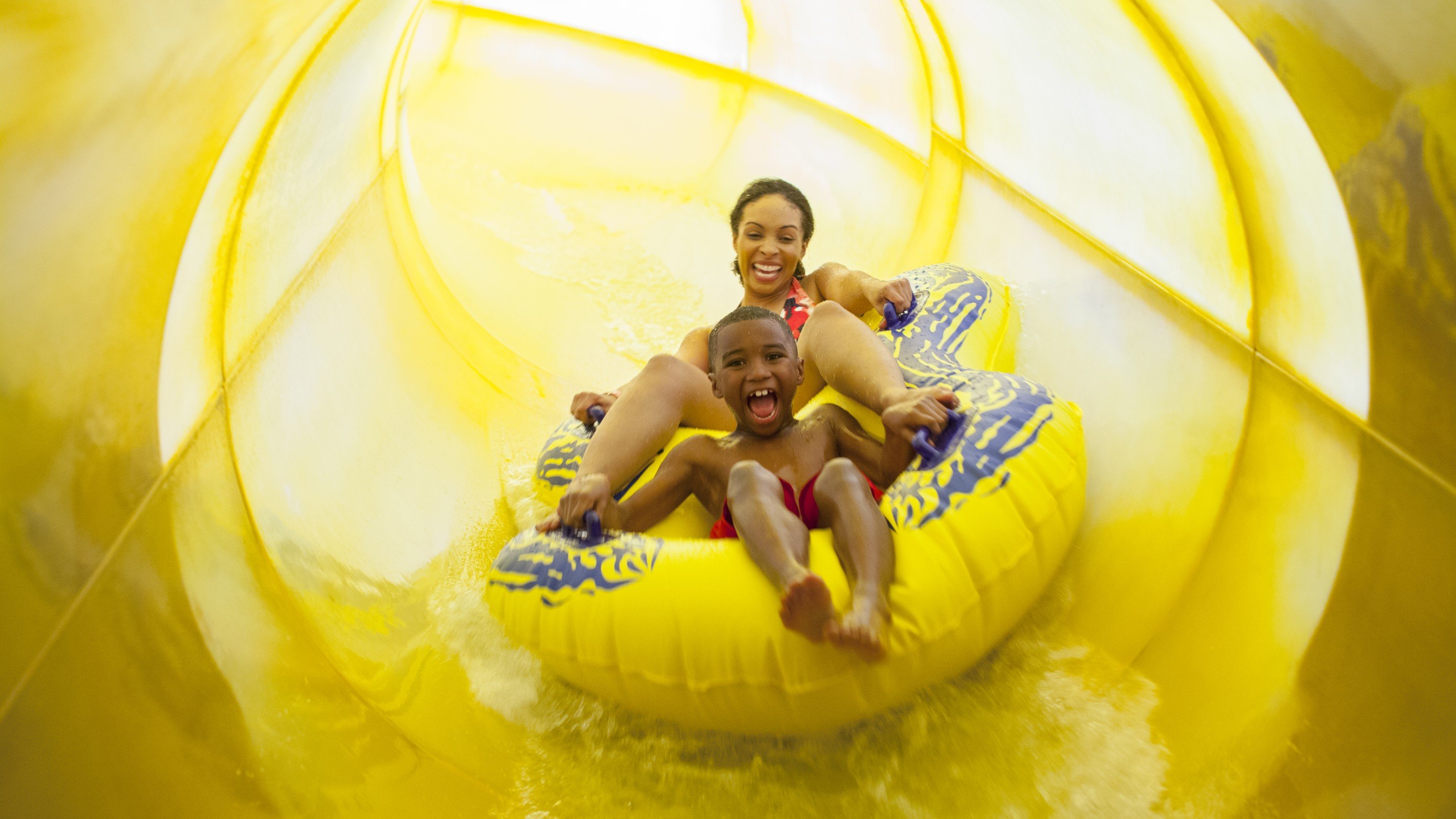 A mother and her son on a yellow tube going down a water slide