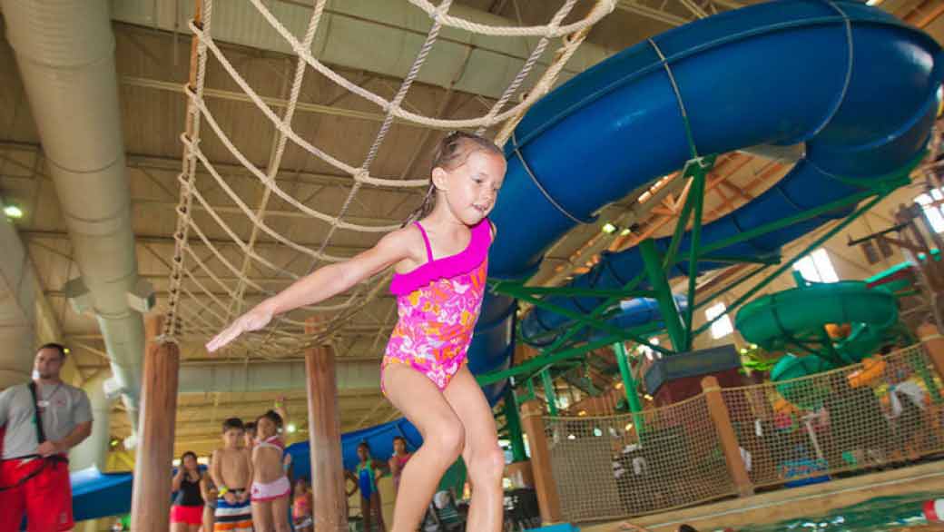A girl balances herself on a cargo net in the Frog Bog Log Walk pool at Great Wolf Lodge indoor water park and resort.