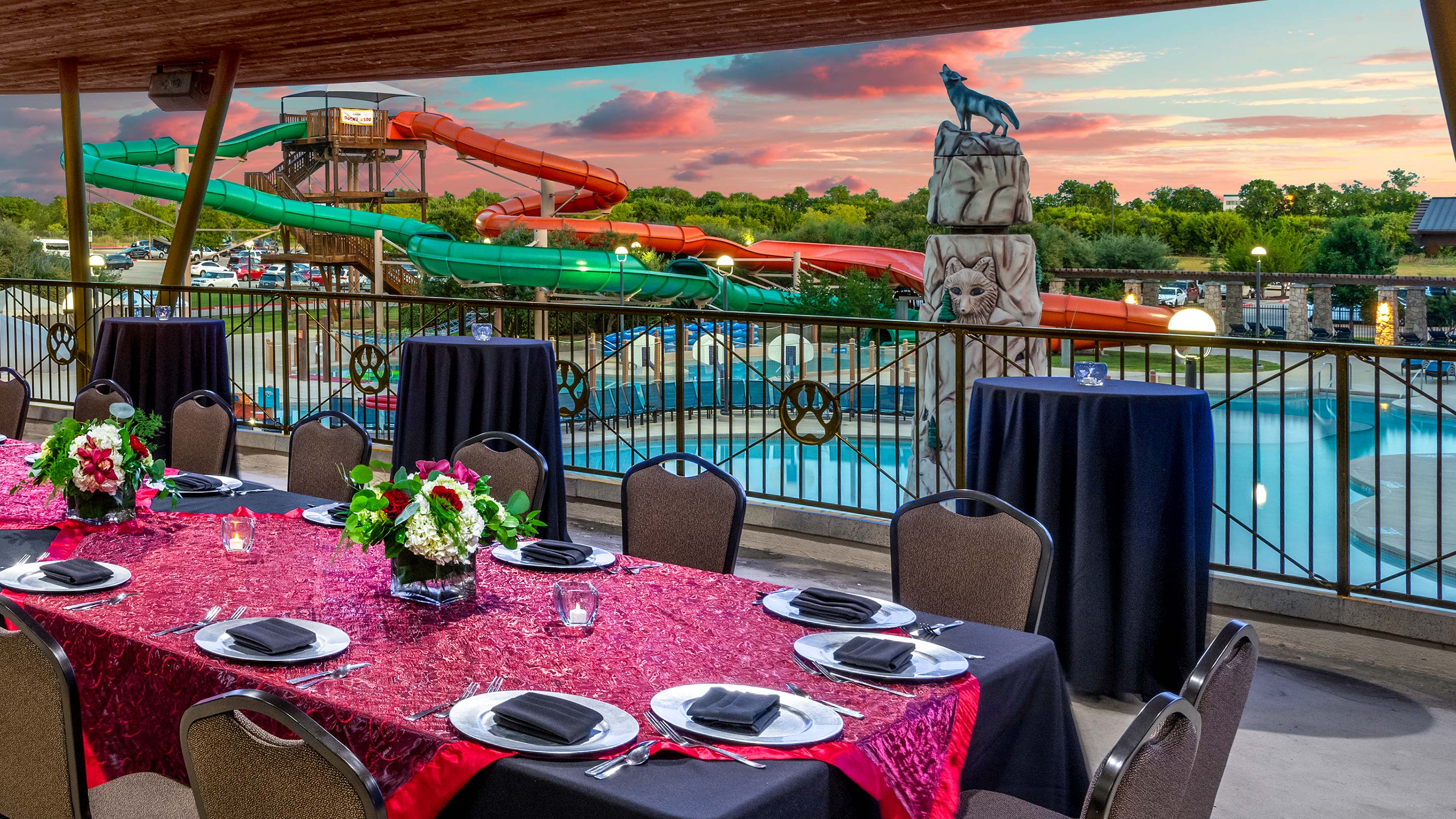 view of an outdoor pool with water slides during summer sunset